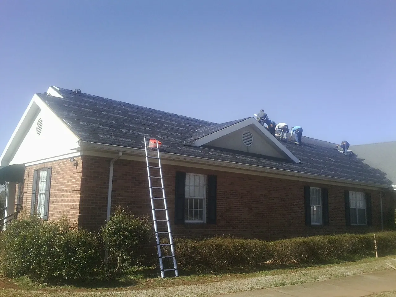 Crew tearing shingles off a brick ranch roof with a ladder set — Emergency Roof Repair work by our crew in Oakdale