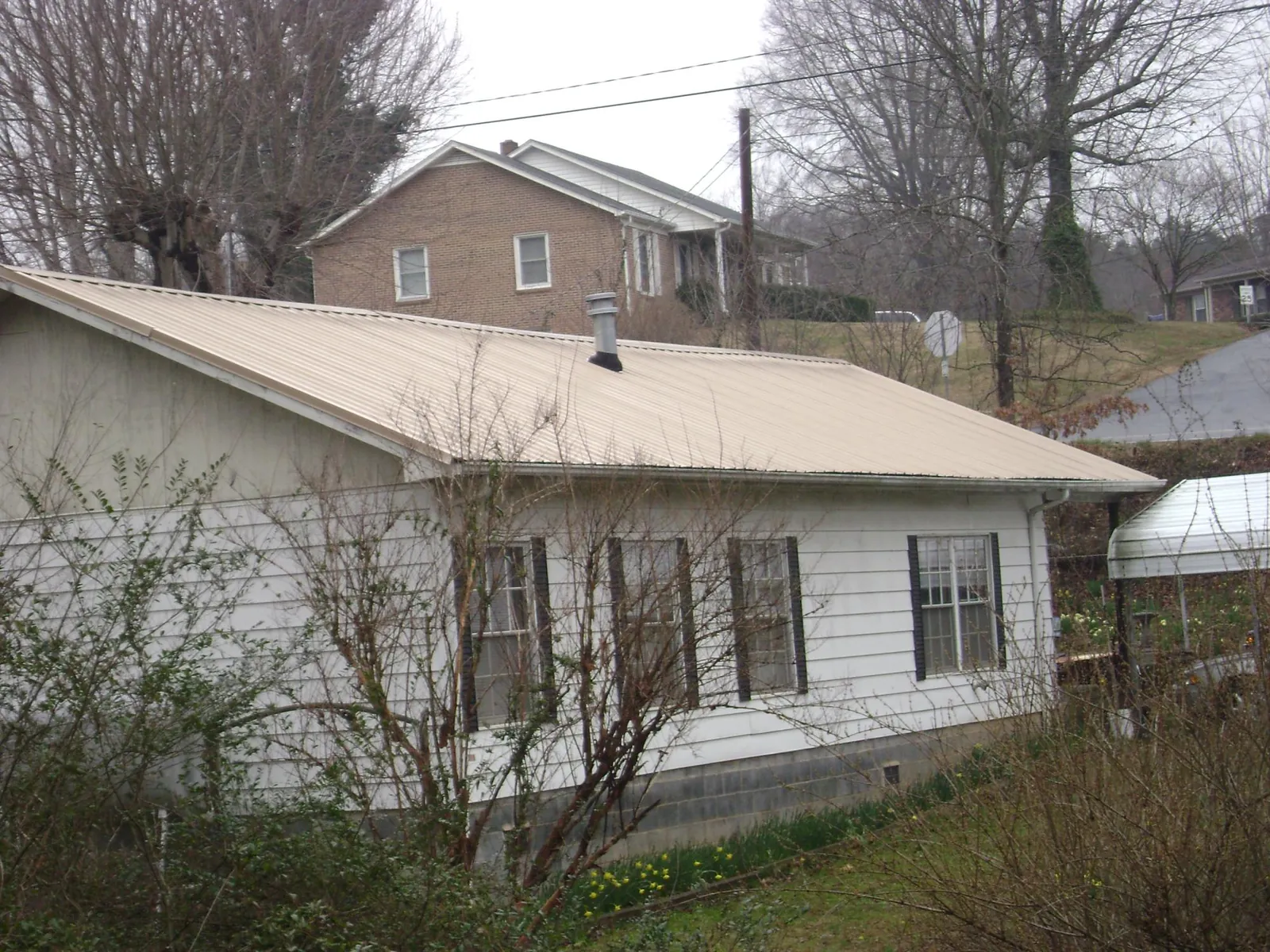 Tan metal roof on a white sided house set into a hillside — Commercial Roofing by Roofing Brothers in Oakdale